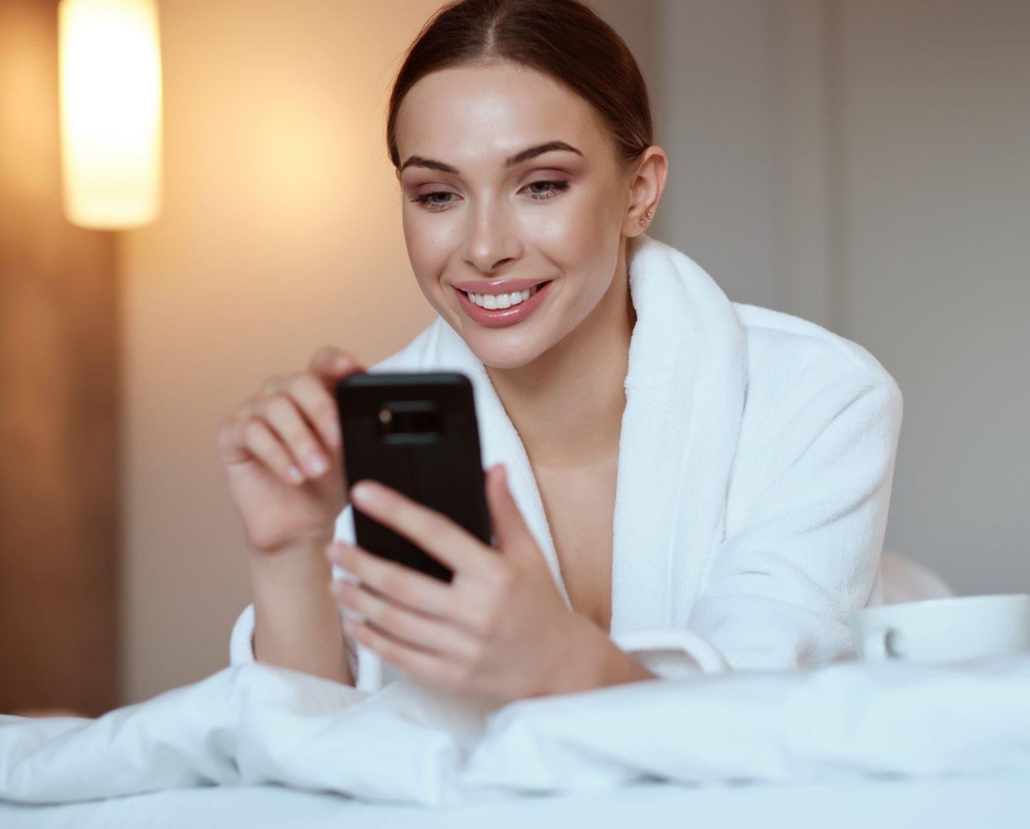 Woman smiling while using smartphone in cozy setting.
